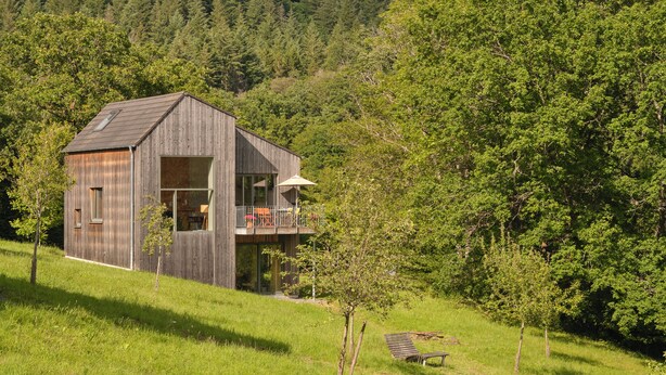 A wooden cabin with a balcony, surrounded by lush greenery and trees. - Architect-designed house, wooden house on a 10,000 m² lot of meadows and woods with a panoramic view (Schutz)