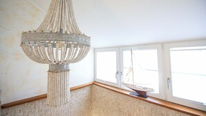 En kristallkrona med flera våder av pärlor som hänger ner från en central punkt, ett fönster med en modell av en segelbåt och en vägg med en intressant yta.