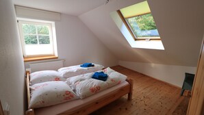 A small, cozy room with a wooden bed, a window with a view of greenery, and a slanted ceiling.