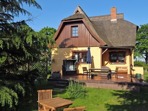 Ein Haus mit geneigtem Dach, einer Holzveranda und einem kleinen Garten mit Tisch und Stühlen.
