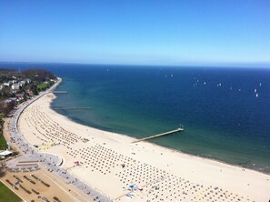 Ein Luftbild eines Strandes mit mehreren Reihen Sonnenliegen und einem Steg, der sich ins Wasser erstreckt.