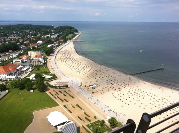 A coastal cityscape with a wide beach, a pier, and residential buildings.