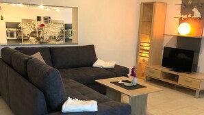 En moderne stue med en mørk sofa, et sofabord, et fjernsyn og et dekorativt spejl.