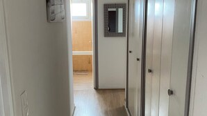 Ein Korridor mit Holzboden, einer Tür mit Spiegel und einer Deckenleuchte.