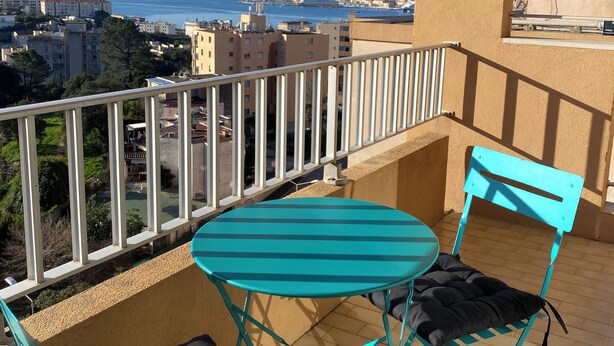 Ein Balkon mit Tisch und Stühlen, der Blick auf das Meer und die Stadt bietet.