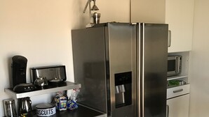 Eine kompakte Küche mit einem Edelstahl-Kühlschrank, einer Mikrowelle, einer Kaffeemaschine und einer kleinen Arbeitsfläche mit einer Keksdose.