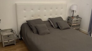 Ein ordentlich bezogenes Bett mit einem gepolsterten Kopfteil, ein Nachttisch mit einer Lampe und ein Holzboden.