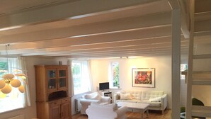 A spacious living room with a wooden dining table, white sofas, and a large window providing natural light. - House for 5 persons, old farmhouse with luxe bathroom, 3 sleeping rooms (Groet)