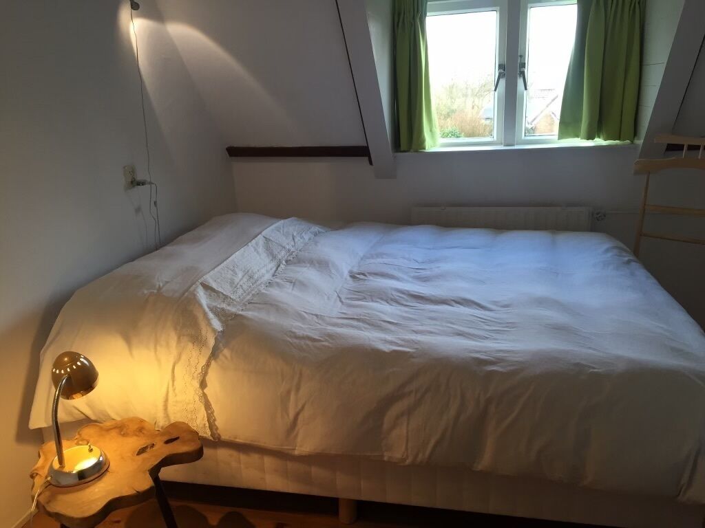 Een slaapkamer met een bed, een bureaulamp, een raam met gordijnen en een houten ladder.