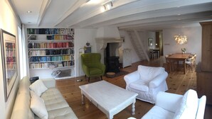 A spacious living room with a fireplace, a bookshelf filled with books, a green armchair, and a white sofa. - House for 5 persons, old farmhouse with luxe bathroom, 3 sleeping rooms (Groet)
