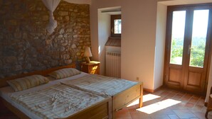Camera da letto con parete in pietra, letto a baldacchino, porta in legno e vista su vegetazione.
