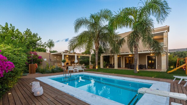 Ein Pool mit Holzboden, umgeben von Palmen und einem Haus.
