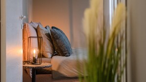 Ein gemütliches Zimmer mit einem Bett, Kissen, einem Nachttisch mit Lampe und einem Fenster mit Blick.