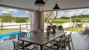Eine Terrasse im Freien mit Pool, Esstisch, Stühlen und Topfpflanzen.