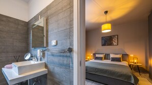Ein modernes Badezimmer mit großem Spiegel, Waschbecken und Handtuch. Der Raum verfügt über eine Holzvertäfelung und ein Bett mit Kopfteil.