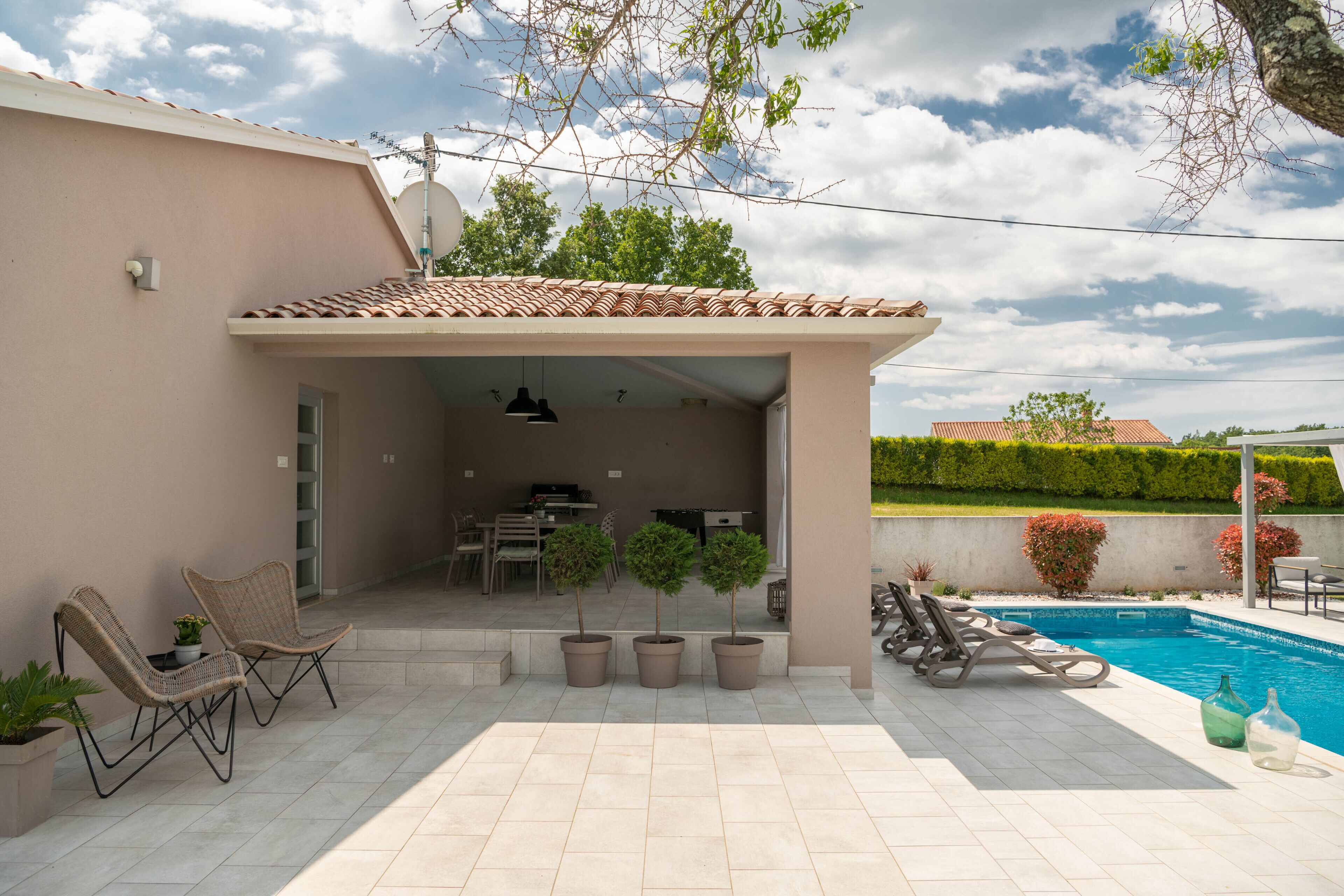 Eine überdachte Terrasse mit Gartenmöbeln, einem Pool und Blumentöpfen.