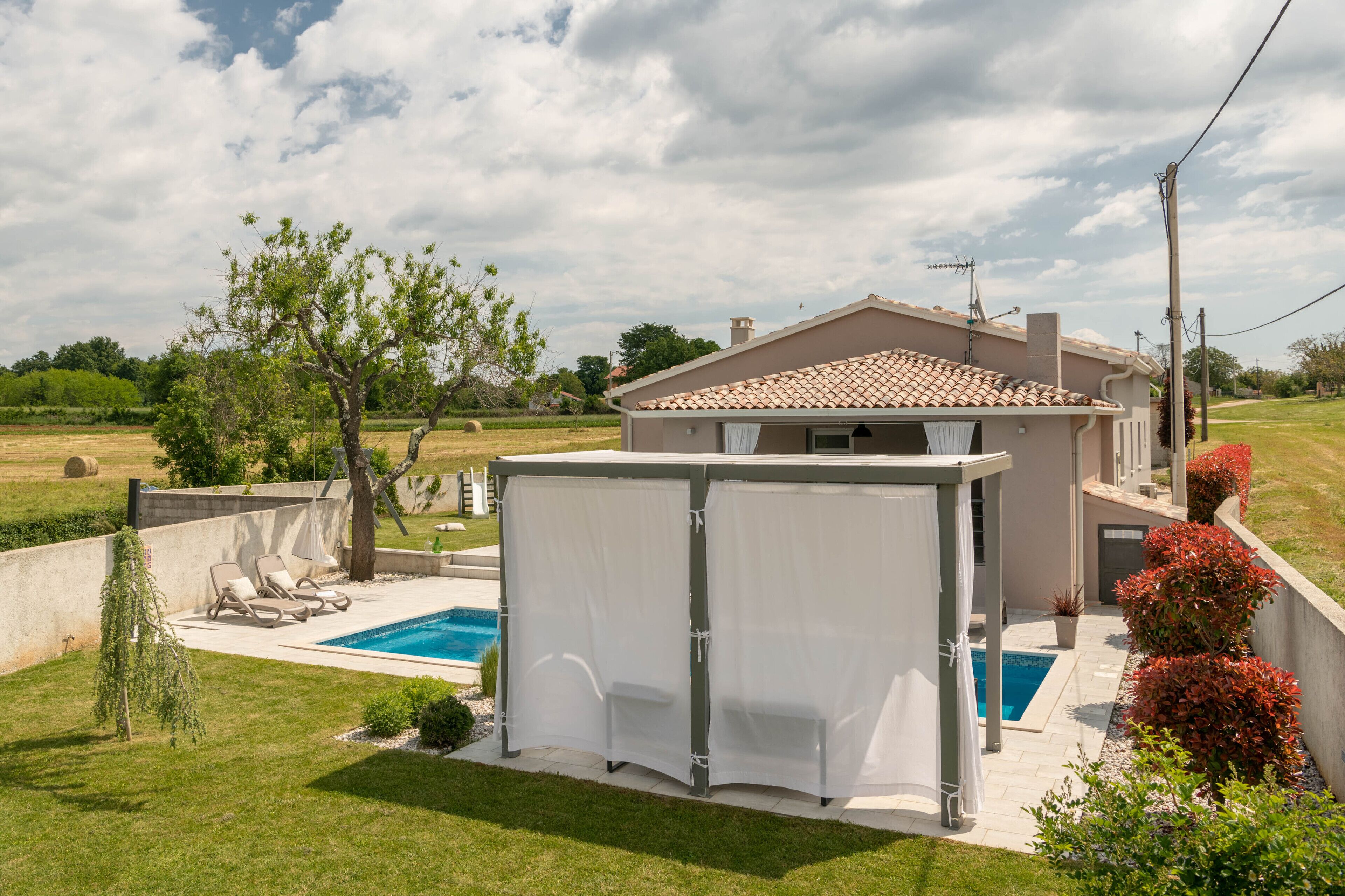 Una casa con piscina, zona de estar exterior cubierta y jardín.