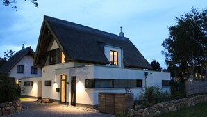 Une maison moderne à deux étages, dotée d’un toit en pente, d’un mur en pierre et d’une allée gravillonnée.