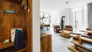 Un mur en bois avec des crochets et une enseigne, un coin salon confortable avec un canapé et une table basse, et une grande fenêtre avec des rideaux.