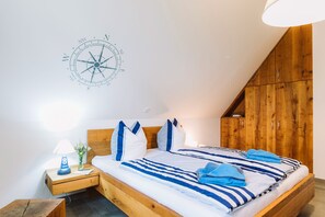 Un dormitorio con cabecera de madera, cama con ropa de cama azul y blanca, mesita de noche con lámpara y decoración de brújula en la pared.
