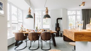 Une cuisine moderne avec un îlot central en bois, des suspensions noires et un coin repas avec des chaises marron.