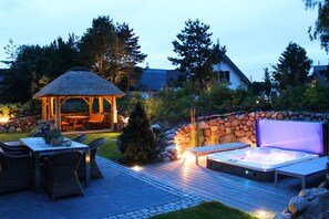 Un área de patio exterior con un jacuzzi, una terraza de madera y un pabellón.