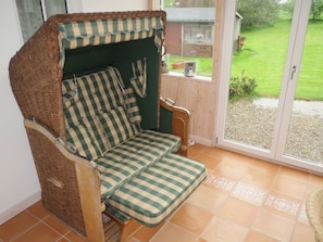 A wicker chair with a checkered cushion in a room with a sliding glass door leading to a garden. - Cozy Swedish house with fireplace, sauna, winter gardens, WLAN New!!! (Biendorf)