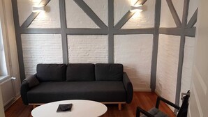A modern living room with a dark grey sofa, a white coffee table, and a black armchair. The room features exposed brick walls and wooden beams. - Located in the heart of Flensburg, in an alley next to the pedestrian zone (Flensburg)