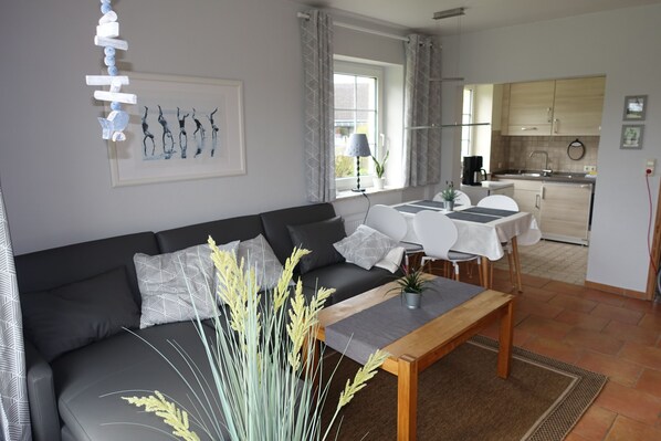A modern living room with a sofa, a dining table, and a kitchen in the background. - Friedrichskoog-Spitze, dike view, quiet location, short distances, family friendly (Friedrichskoog)