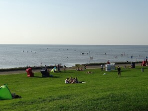 A grassy area with a view of the sea, a red play structure, and a green tent. - Friedrichskoog-Spitze, dike view, quiet location, short distances, family friendly (Friedrichskoog)