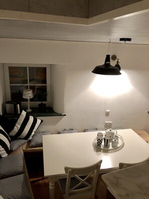 Et hyggeligt spiseområde med et hvidt bord, ternede puder og en sort hængende lampe.