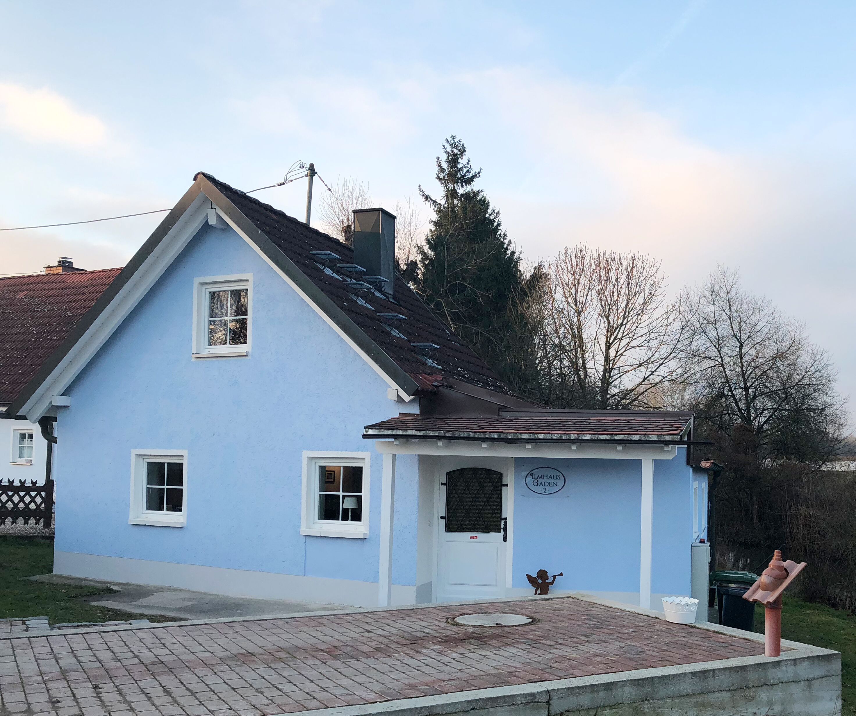A light blue building with a sloped roof, a small porch, and a door with a sign above it.
