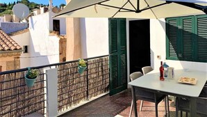 A balcony with a table, chairs, a large umbrella, and potted plants. - Centrally located in Pollensa with wonderful roof terrace views (Pollença)