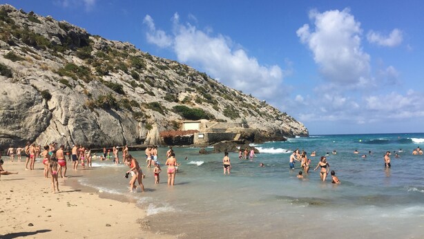 A beach with clear waters, rocky cliffs, and a few people swimming and sunbathing. - Centrally located in Pollensa with wonderful roof terrace views (Pollença)
