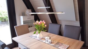 Ein Essbereich mit einem Holztisch, einer Vase mit rosa Blumen und einer modernen Pendelleuchte.