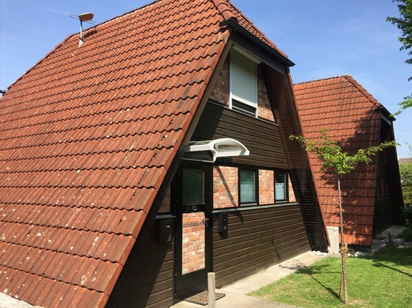 Ein zweistöckiges Haus mit geneigtem Dach, Schornstein und kleinem Garten.