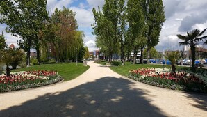 Ein Weg, der von Blumenbeeten und Bäumen gesäumt wird und zu einem Gebäude mit rotem Dach führt.