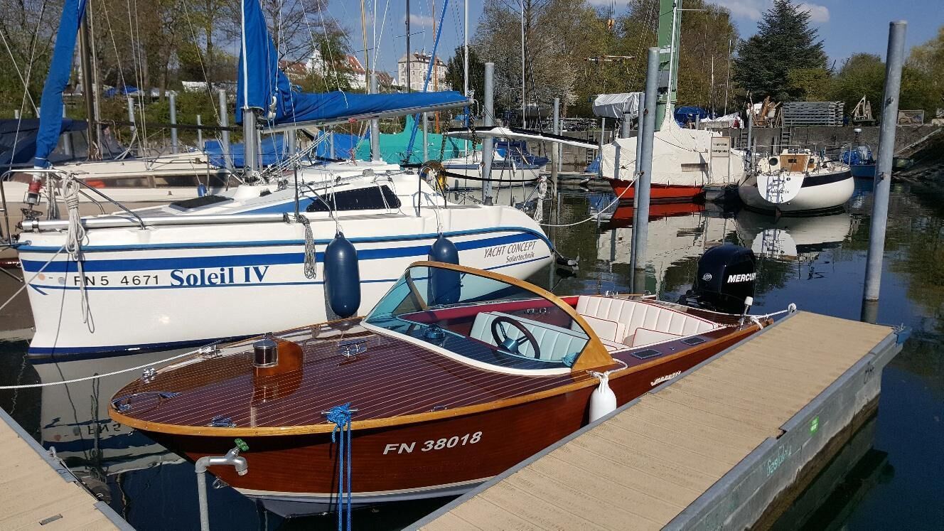 Un port de plaisance où sont amarrés des bateaux, dont un bateau en bois sur lequel on peut lire les inscriptions « Yacht Concept » et « Soleil IV » sur le côté.