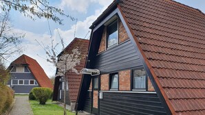 Ein modernes, zweistöckiges Haus mit Satteldach, Backsteinfassade und einem kleinen Vorgarten mit einem Weg und einem Busch.