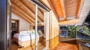 Une chambre moderne avec un plafond en bois, une porte coulissante en verre donnant sur un balcon, et un lit avec des oreillers et une couverture.