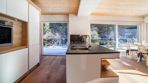 Une cuisine moderne avec un plafond en bois, de grandes fenêtres et un coin repas avec des chaises.