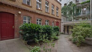 Un cortile con una porta rossa, edifici in mattoni e piante verdi.