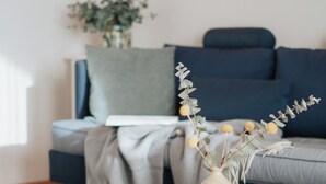 A living room with a blue sofa, a small wooden table with a vase, and a dark blue rug with leaf patterns.