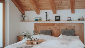 A bedroom with a wooden headboard, a bedside table with a lamp, and a shelf with decorative items.