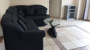 Un salon avec un canapé d’angle noir, une table basse en verre et une tête de cerf décorative.