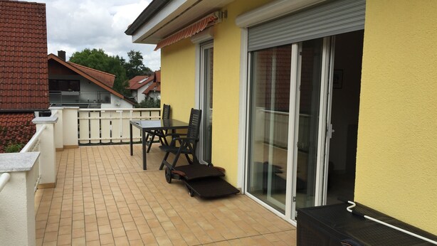 Une terrasse avec une table et des chaises, une porte-fenêtre coulissante et un barbecue.