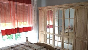 Une chambre à coucher avec un lit, une armoire en bois dotée de portes en verre et une fenêtre ornée de rideaux légers.