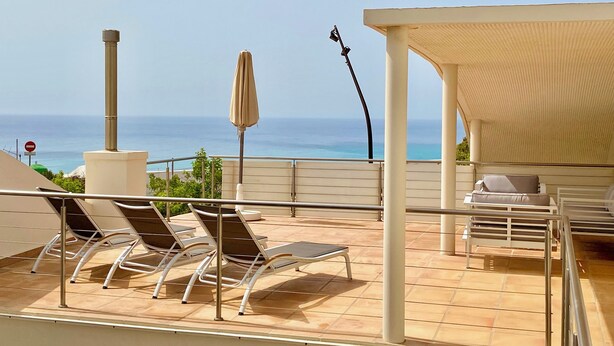 Une terrasse sur le toit avec des chaises longues, un espace salon couvert et une vue sur l’océan.