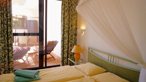 Une chambre d’hôtel avec un lit, une fenêtre avec des rideaux, une chaise et une table avec une lampe.