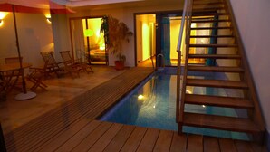 Un espace piscine doté d’un sol en bois, d’un escalier et d’un coin salon avec des chaises et une table.